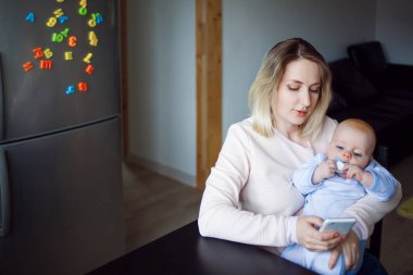 Genç anne bebekle oturur ve telefon kullanır. Internet tarama, kapalı