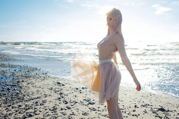 Vrolijk meisje aan de kust. Jonge blonde vrouw die lacht. Trendy beige rok — Stockfoto