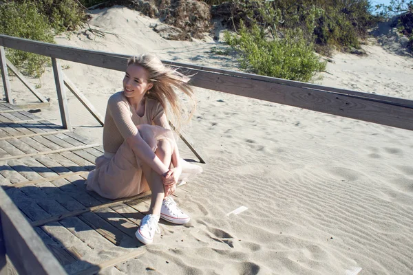 Joven chica alegre en la orilla del mar. Mujer rubia joven sentada en la arena y disfrutando del buen tiempo —  Fotos de Stock