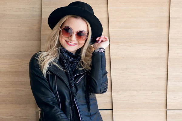 Drôle et belle blonde dans des lunettes de soleil et un chapeau. Portrait fille à la mode en plein air. Rires et tient le chapeau — Photo