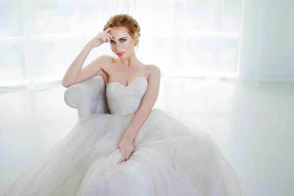Portret van een mooi meisje in een trouwjurk. Bruid in luxe jurk zittend op een stoel — Stockfoto