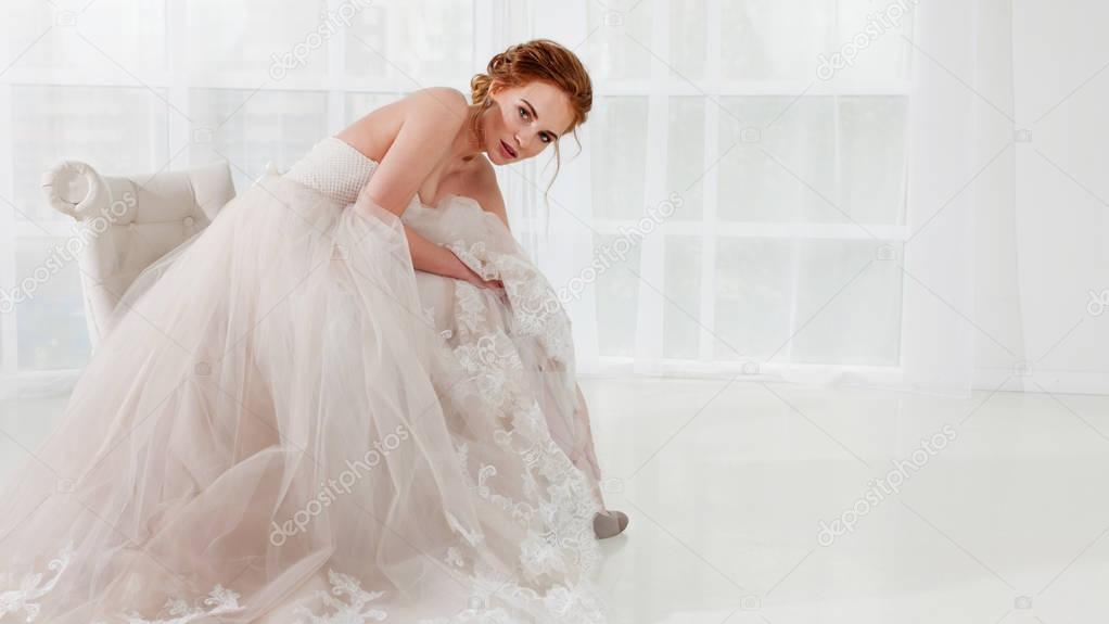 Portrait of a beautiful girl in a wedding dress. Bride in luxurious dress sitting on a chair