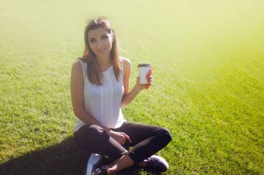 Female sitting on the grass drinking coffee in a cardboard Cup clipart
