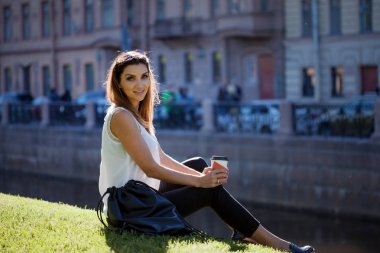 Karton bir fincan kahve içme çimenlerin üzerinde oturan kadın