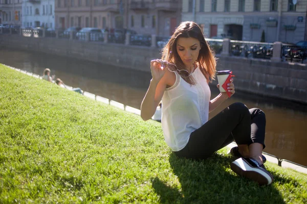 Karton bir fincan kahve içme çimenlerin üzerinde oturan kadın — Stok fotoğraf