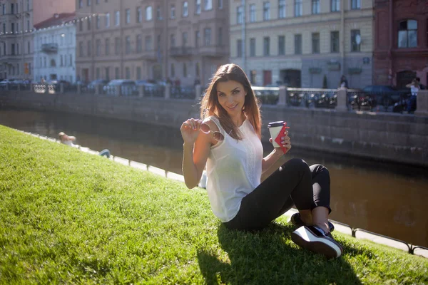 Frau sitzt auf dem Gras und trinkt Kaffee in einem Pappbecher — Stockfoto