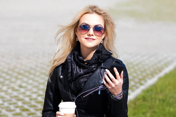 Chica de moda retrato al aire libre. Un paseo por la ciudad. Mujer joven utiliza el teléfono y beber café —  Fotos de Stock