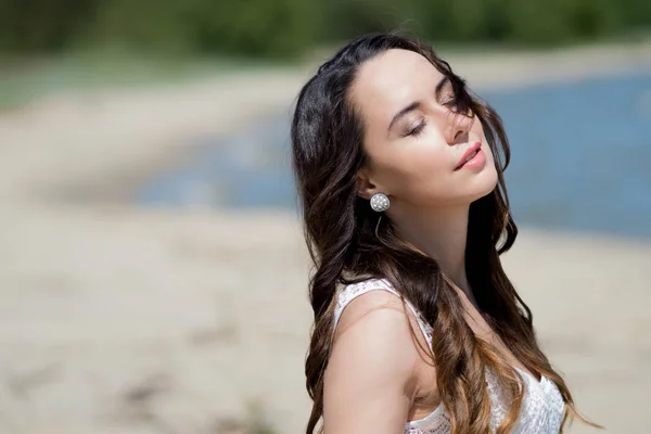 Jeune belle femme brune en robe blanche sur le bord de mer. portrait avec les yeux fermés — Photo