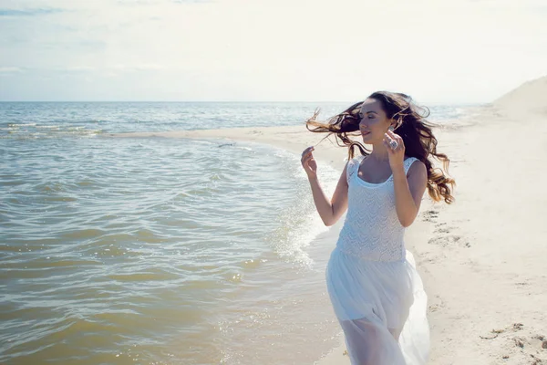 Young beautiful brunette woman in white dress on the seashore — Stock Photo, Image