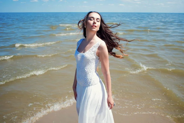 Joven mujer morena hermosa en vestido blanco en la orilla del mar — Foto de Stock