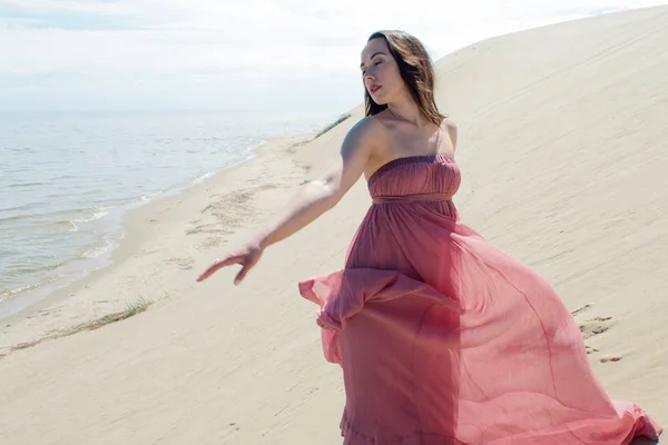 Donna in abito rosso ondulante con tessuto volante corre su sfondo di dune — Foto Stock