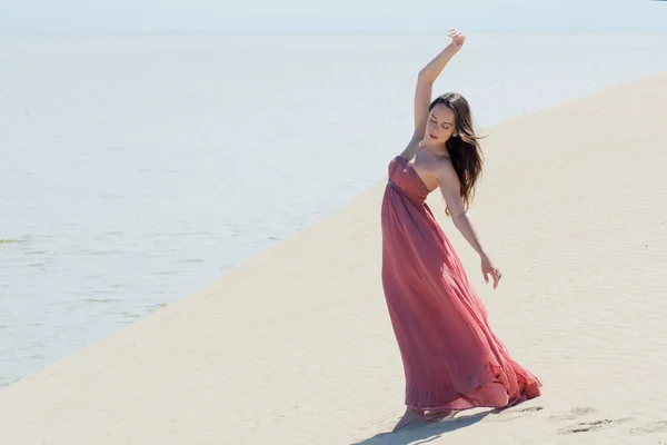 Mujer en vestido ondulante rojo con tela voladora se ejecuta en el fondo de las dunas — Foto de Stock