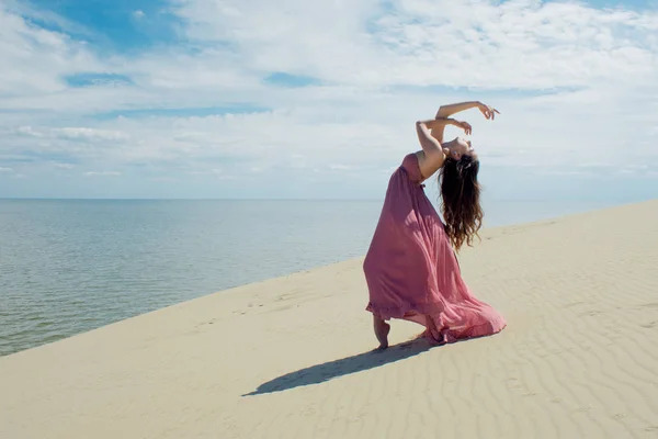 Mujer en vestido ondulante rojo con tela voladora se ejecuta en el fondo de las dunas. Gimnasta en la parte posterior de la duna — Foto de Stock