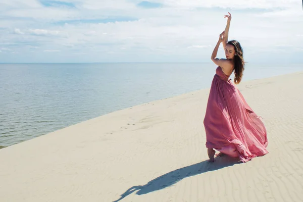 Mujer en vestido ondulante rojo con tela voladora se ejecuta en el fondo de las dunas. Gimnasta en la parte posterior de la duna — Foto de Stock