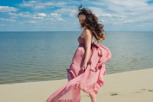 Žena v Rudém mávali šaty s létáním tkaniny běží na pozadí dun. Panorama a moře — Stock fotografie