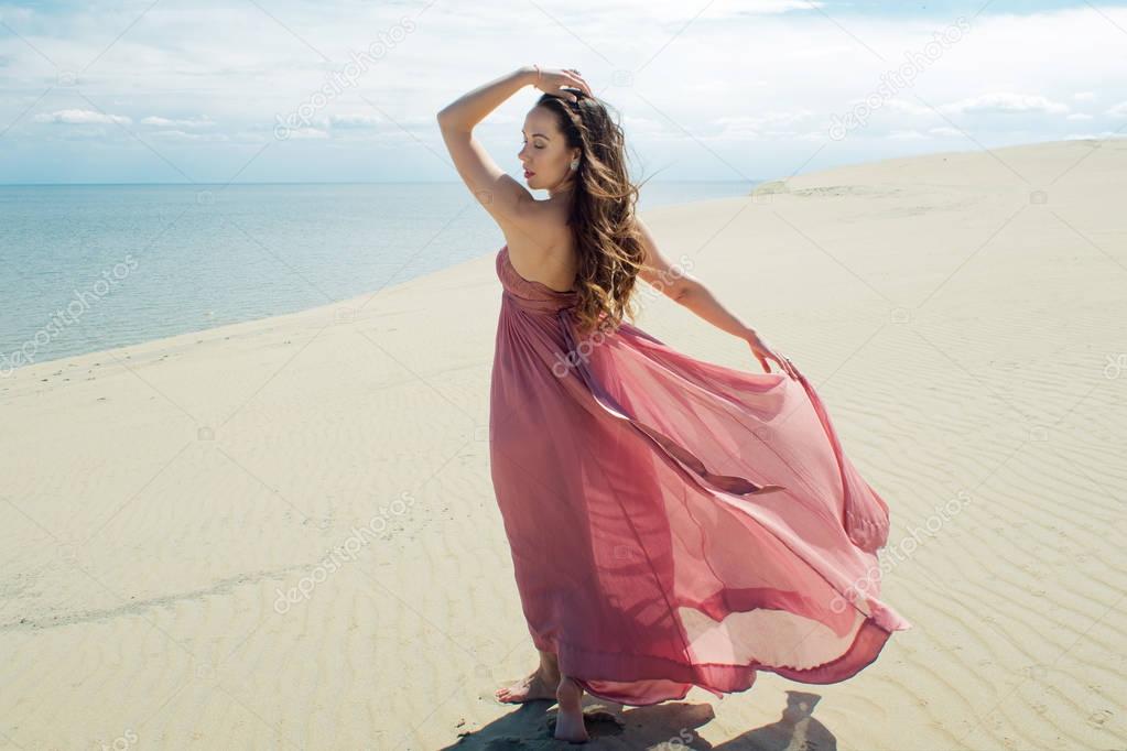 Woman in red waving dress with flying fabric runs on background of dunes