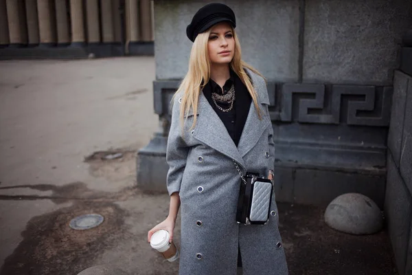 Модна блондинка гуляє з кавою, щоб піти, жінка в стильному капелюсі і сірому пальто — стокове фото
