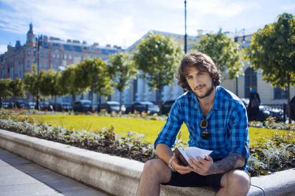 Un tipo con camisa azul leyendo un libro. Retrato de un joven guapo y elegante en la calle . — Foto de Stock