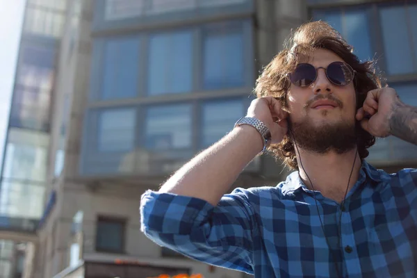 Парень в солнечных очках наслаждается музыкой. Портрет молодого красивого стильного мужчины на улице . — стоковое фото