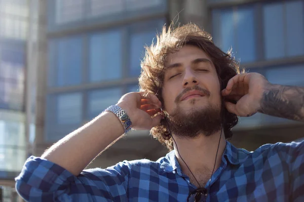 Skäggig kille njuta av musiken. Porträtt av ung stilig snygga mannen på gatan. — Stockfoto