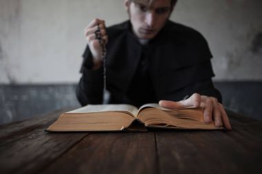 Sayfa İncil, yakın çekim. Yakışıklı genç Katolik rahip portresi. El ele