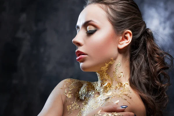 Menina morena bonita com imagem criativa com folha de ouro no pescoço. Retrato de estúdio sobre um fundo escuro . — Fotografia de Stock