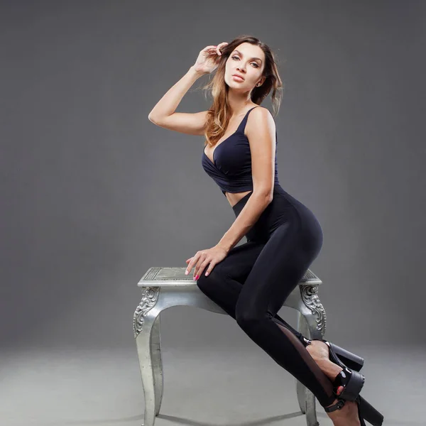 Belle femme brune sexy assise sur une chaise. Portrait sur fond gris — Photo