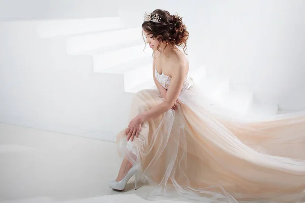 Menyasszony a lépcsőn ül. Portréja egy gyönyörű lány, egy esküvői ruha. Tánc a menyasszony, fehér háttér. — Stock Fotó