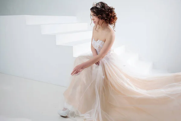 Bride sits on the stairs. Portrait of a beautiful girl in a wedding dress. Dancing Bride, white background. — Stock Photo, Image