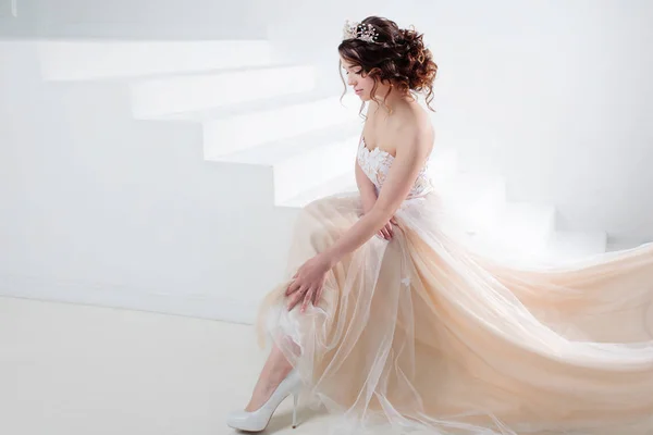La novia se sienta en las escaleras. Retrato de una hermosa chica en un vestido de novia. Novia Bailarina, fondo blanco . —  Fotos de Stock