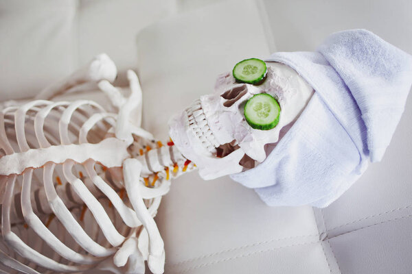 Скелет в салоне Спа с полотенцем на голове и маской на лице, расслабляет, заботится о себе. Абсурдная концепция, социальная пародия. Заботься о красоте и забудь о внутреннем мире
