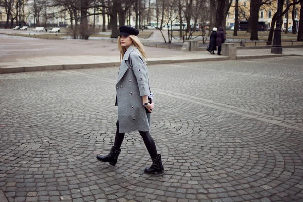 Genç, kalça ve çekici sarışın kız şık bir şapka ve gri bir ceket şehirde yürüyüş. Yaya geçidi