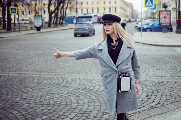 Young, hip and attractive blonde hailing taxi , girl in a stylish hat and a gray coat — Stock Photo, Image