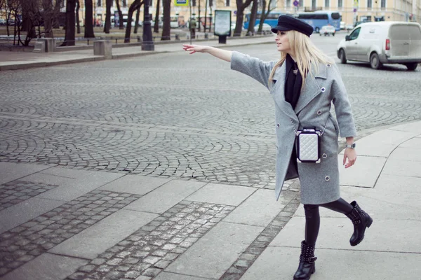 Jeune, hanche et attrayant taxi d'accueil blonde, fille dans un chapeau élégant et un manteau gris — Photo