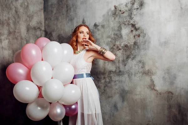 Roodharige schoonheid jonge vrouw in een witte jurk, houden een grote bundel van ballonnen op het feest. — Stockfoto