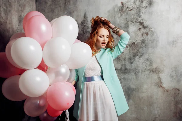 Roodharige schoonheid jonge vrouw in een witte jurk, houden een grote bundel van ballonnen op het feest. — Stockfoto