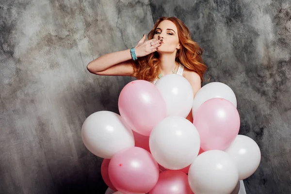 Chica pelirroja bastante joven con globo aéreo envía un beso de aire. Chica pelirroja feliz y alegre. Sobre fondo texturizado gris —  Fotos de Stock