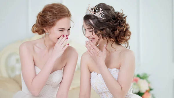 Duas noivas estão sussurrando sobre algo e rindo. Meninas delicadas bonitas em vestidos de noiva . — Fotografia de Stock