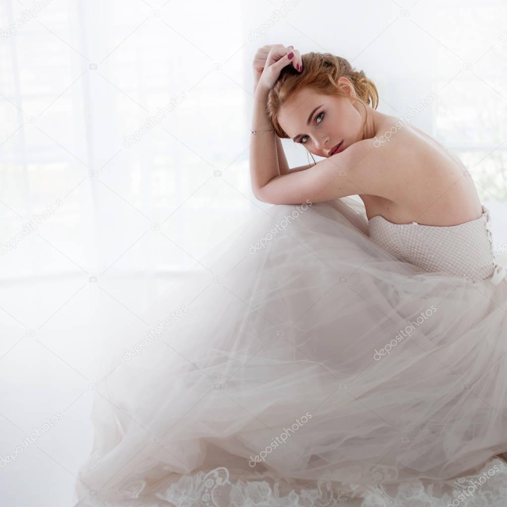 Portrait of a beautiful girl in a wedding dress. Bride in luxurious dress sitting on the floor