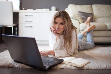 Öğrenci çalışmaları evde. Halı laptop önünde yatan genç güzel kız