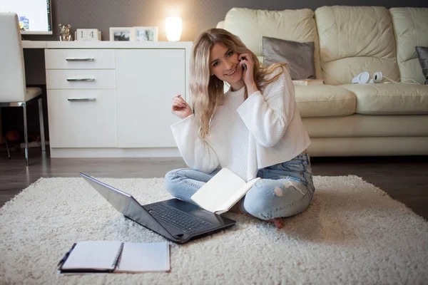 Cute blonde talking on the phone sitting on floor. Work with a laptop, freelance blogger — Stock Photo, Image