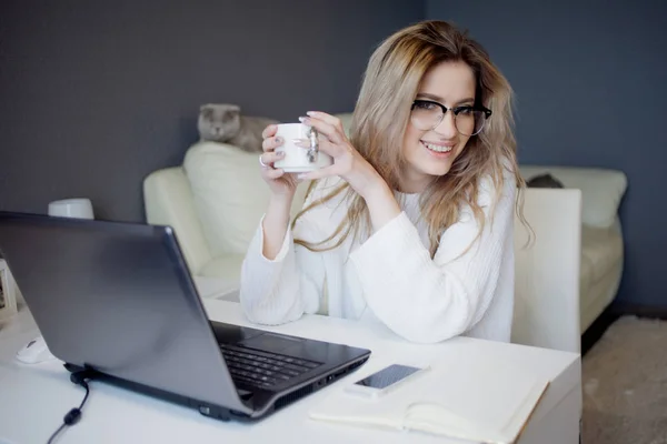 Студент или фрилансер, работающий дома с ноутбуком. Очаровательная молодая женщина сидит перед монитором с чашкой кофе . — стоковое фото