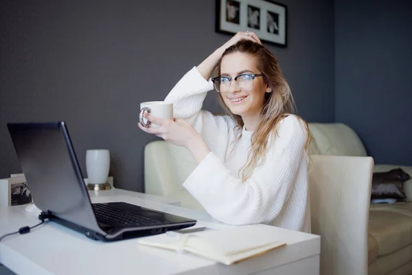 Estudante ou freelancer, trabalhando em casa com laptop. Jovem encantadora senta-se na frente do monitor com xícara de café . — Fotografia de Stock