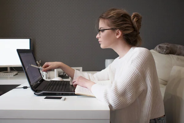 Jonge zakenvrouw kijkt op het scherm. Mooi meisje met bril thuis werken met laptop — Stockfoto