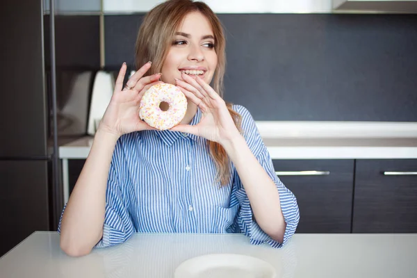 Красивая молодая женщина с пончиком в руке. Девушка на кухонном столе — стоковое фото