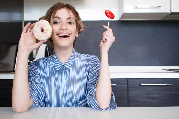 Красивая молодая девушка с пончиком и леденец на кухне . — стоковое фото