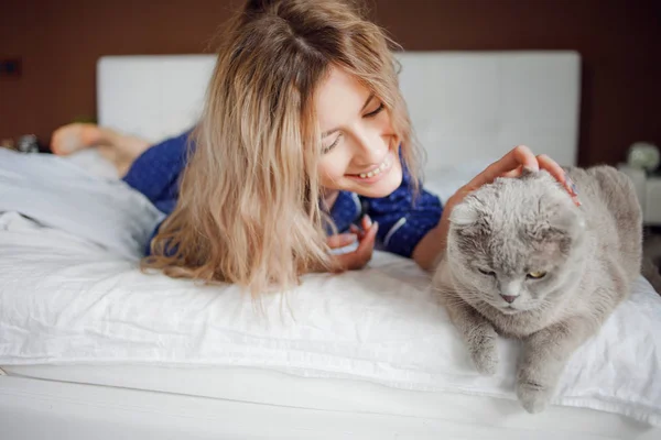 Portrait of a beautiful woman in pajamas at home, lying in bed. Pat the cat