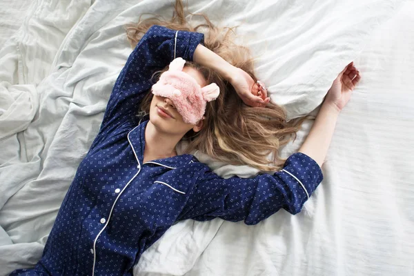 Carino bionda nel suo letto in pigiama blu e maschera del sonno, vista dall'alto — Foto Stock