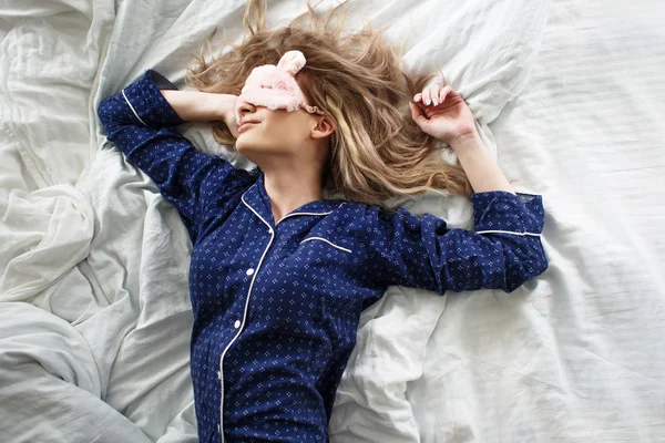 Schattig blond in haar bed in blauwe pyjama en slaapmasker, bovenaanzicht — Stockfoto