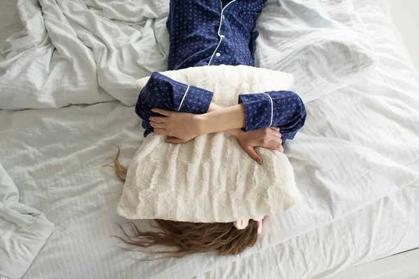 Zu faul, um aus dem Bett zu kommen, bedeckt eine Frau ihr Gesicht mit einem Kissen — Stockfoto